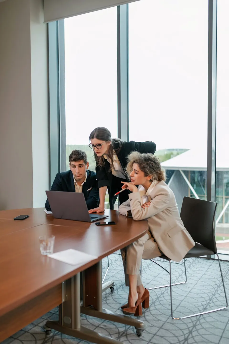 Three colleagues gathered around one laptop at a conference table, talking through work together